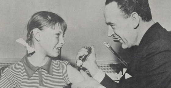 Man administering a vaccine to a smiling girl.